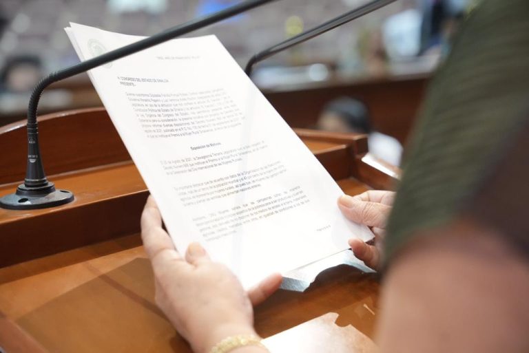 Dos manos sostienen documento que es leído en tribuna.
