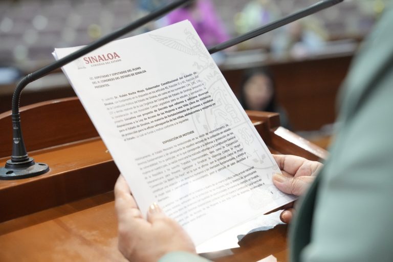 Par de manos sostiene documento que es leído en tribuna.