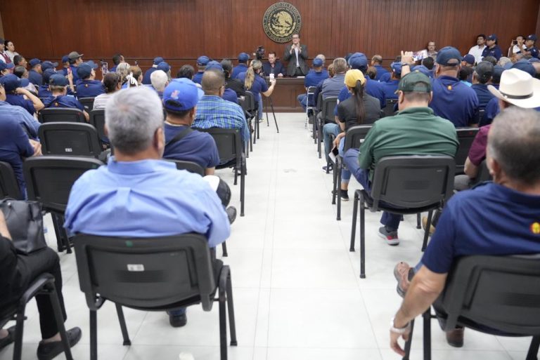 Decenas de policías jubilados y viudas de policías sentadas en sillas. Se ven de espaldas y al fondo diputados que les atienden.