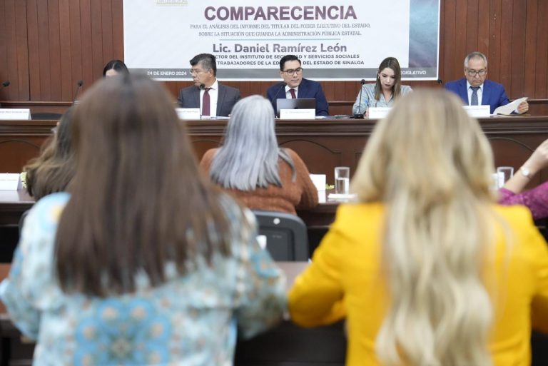 Diputadas aparecen de espaldas en fotografía y al fondo el funcionario compareciente acompañado de diputadas y diputados.