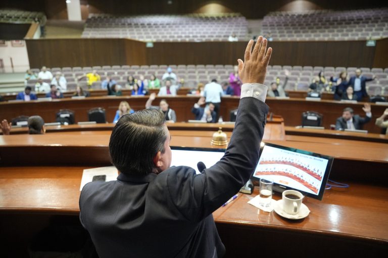 Presidente de la Mesa Directiva vota levantando el brazo. Frente a el hacen lo mismos sus compañeras y compañeros.