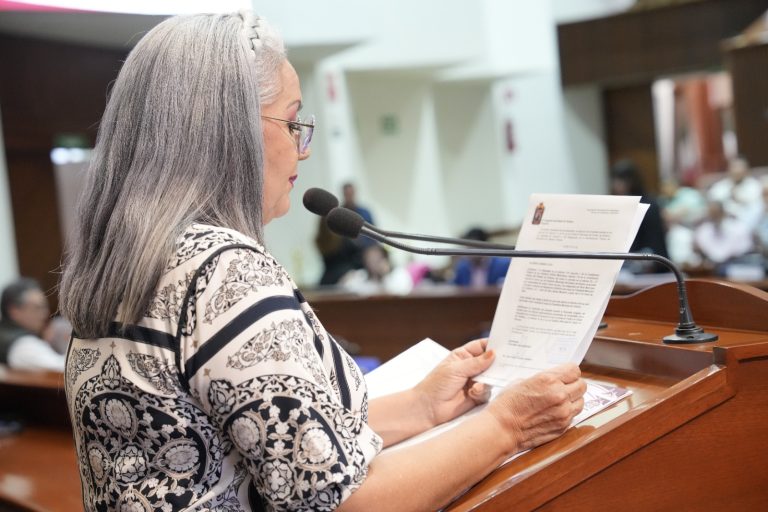 Diputada da lectura a solicitudes de ayuntamientos en tribuna frente a micrófono.