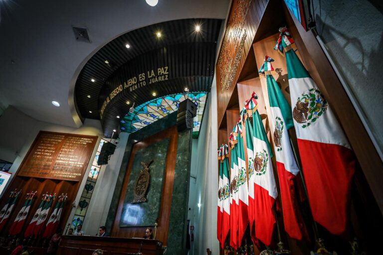 Cuerpo de banderas aparece en primer plano, y al fondo parte de la Mesa Directiva.