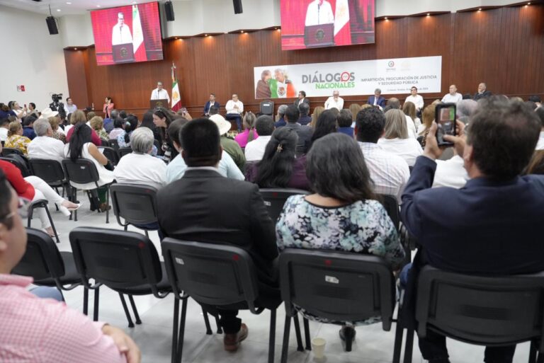 Decenas de personas participan en el evento, sentadas frente al presidium.