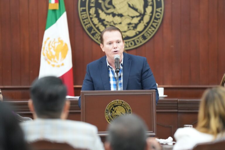 En foto de archivo el diputado Adolfo Beltrán Corrales habla en podium, al dado de una bandera mexicana.