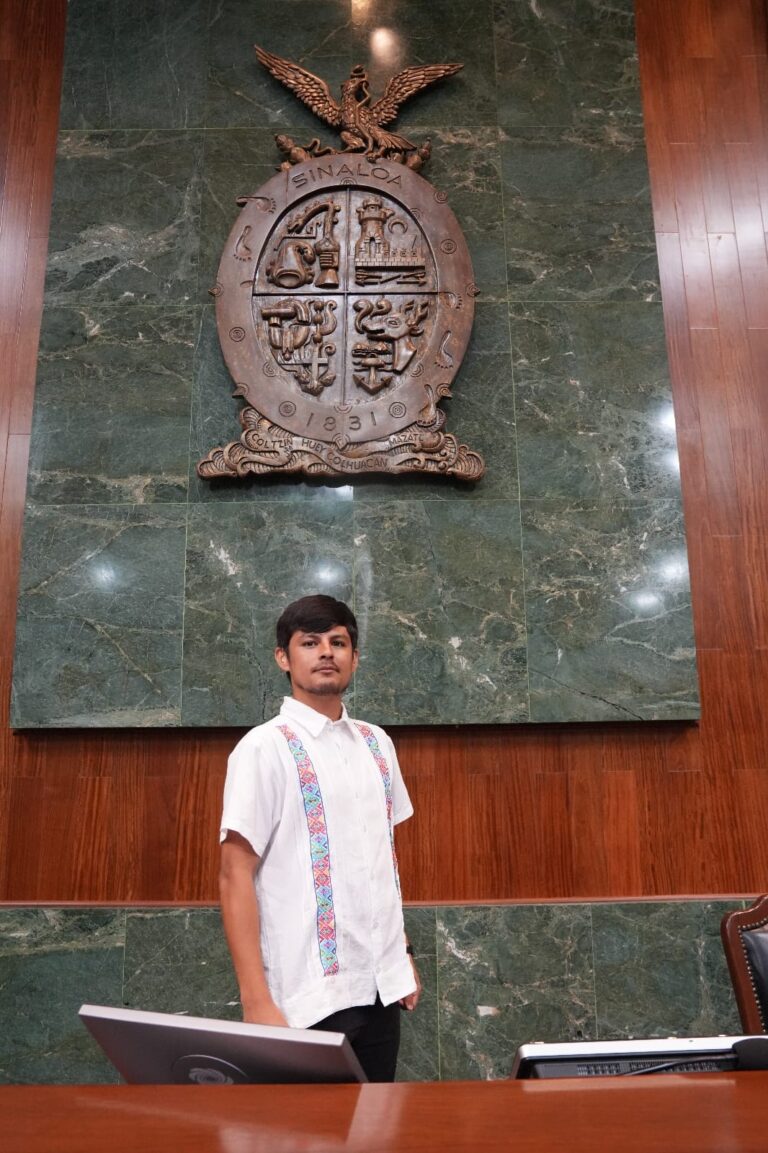 Francisco Alberto Ibarra Fongo posa de pie en el Salón de Sesiones del Congreso, debajo del gran escudo de Sinaloa, hecho de mandera.