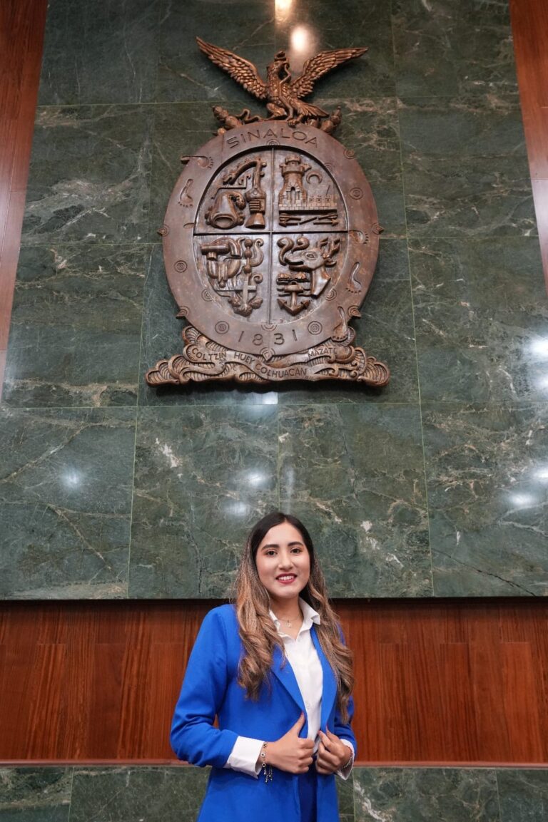 María Guadalupe Beltrán posa bajo el gran escudo de madera de Sinaloa, en el Salón de Sesiones.