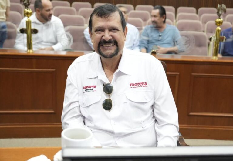 Diputado Serapio Vargas, vestido con camisa blanca, sonríe sentado en su curul.