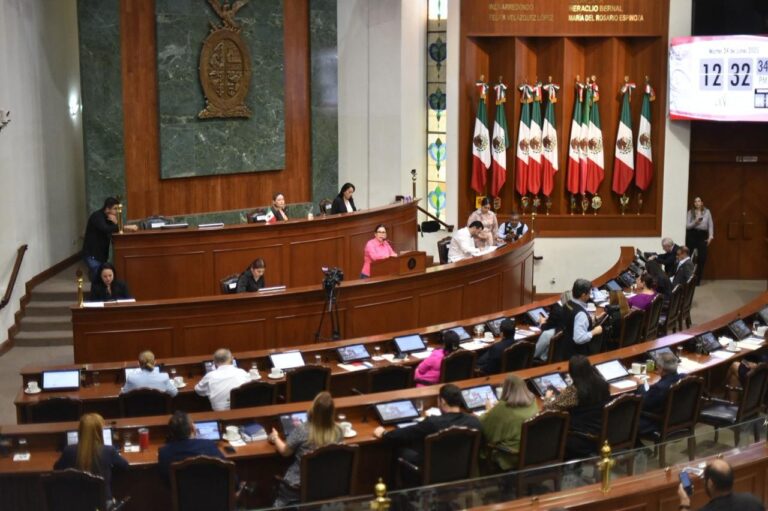 Vista panorámica de diputadas y diputados en sus sillas, y al fondo la Mesa Diretctiva con diputada que habla en ribuna.