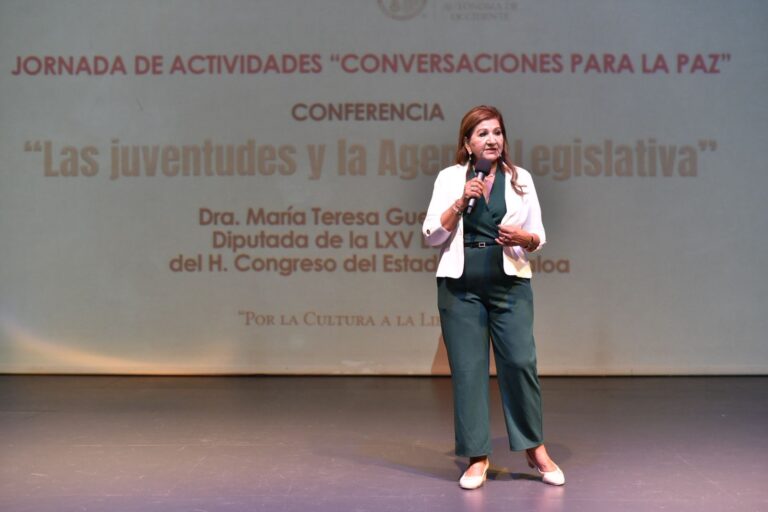 Diputada Tere Guerra de pie en escenario, frente a comunidad de la UAdeO.