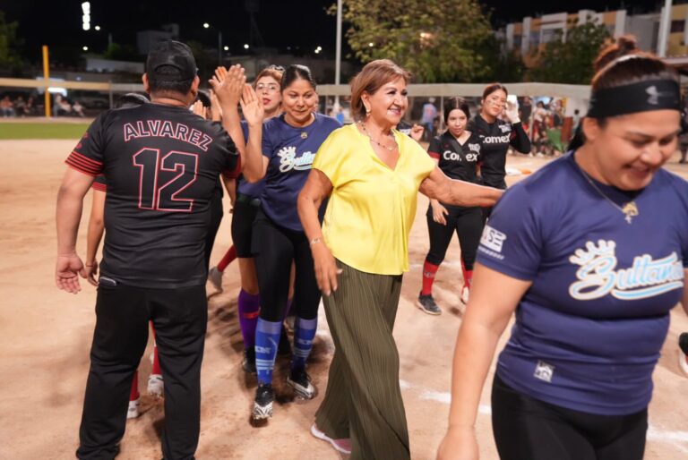 Diputada Tere Guerra camina entre mujers softbolistas en campo de soft.