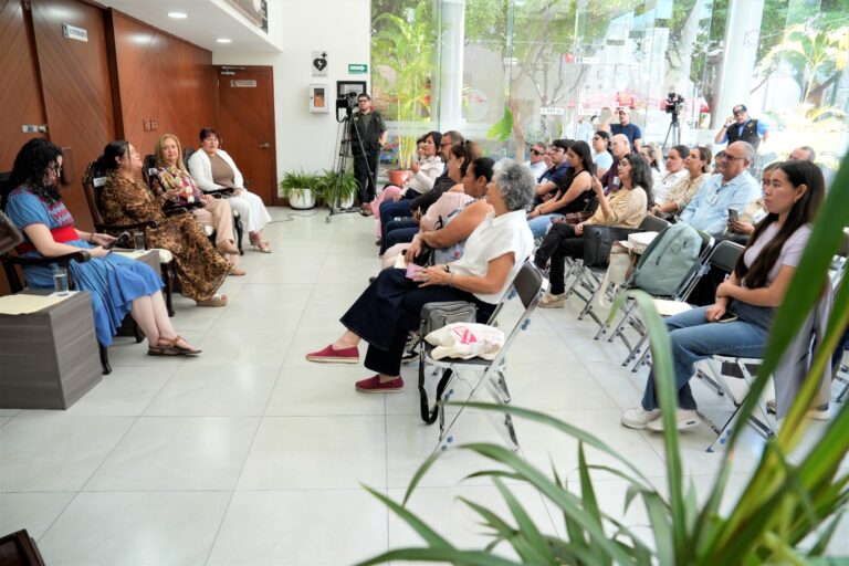 Autora y comentaristas aparecem sentadas frente a público asistente.