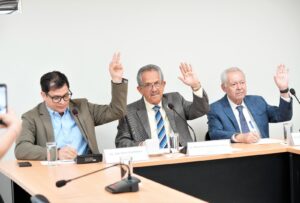 Tres diputados votan levantando sus manos.