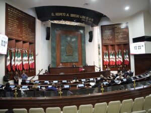 Imagen amplia del Salón de Sesiones, con diputados en sus asientes, Mesa Directiva y lotes de banderas que decoran las paredes laterales.