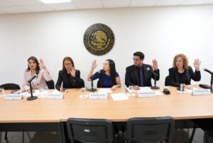 Integrantes de la comisión levantan sus manos al votar.