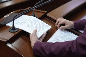 Un par de manos sostiene documento al que se le da lectura en tribuna.