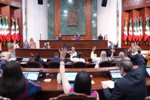 Desde sus asientos, diputados y diputadas votan levantando sus manos durante la sesión ordinaria.