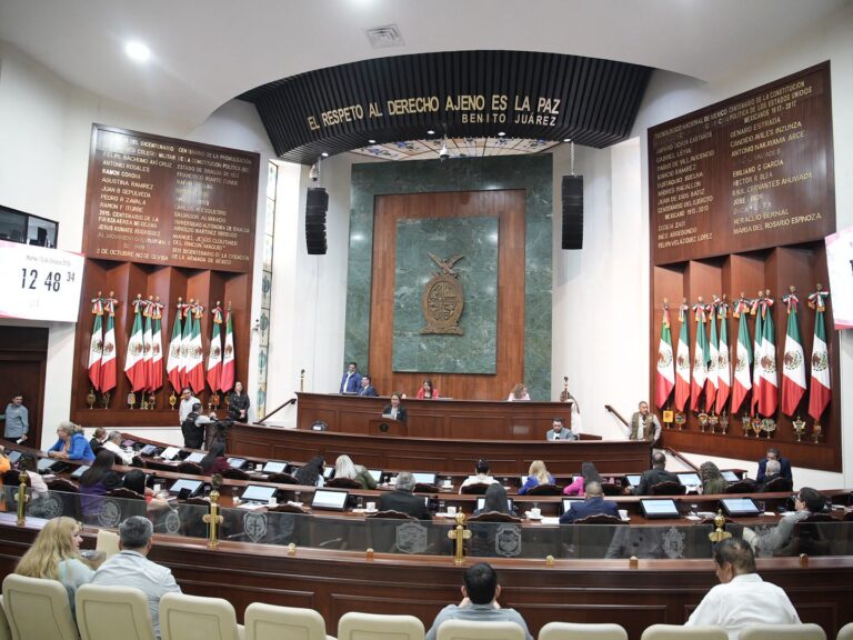Fotografía amplia del Salón de Sesiones. Diputados al centro. Al fondo la Mesa Directiva. A los costados lotes de banderas de México.