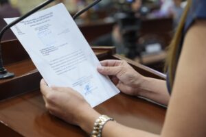 Par de manos de diputada sostiene documento al que se le da lectura en tribuna.