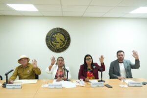 Cuatro integrantes de la comisión, votan sentados levantando sus manos.